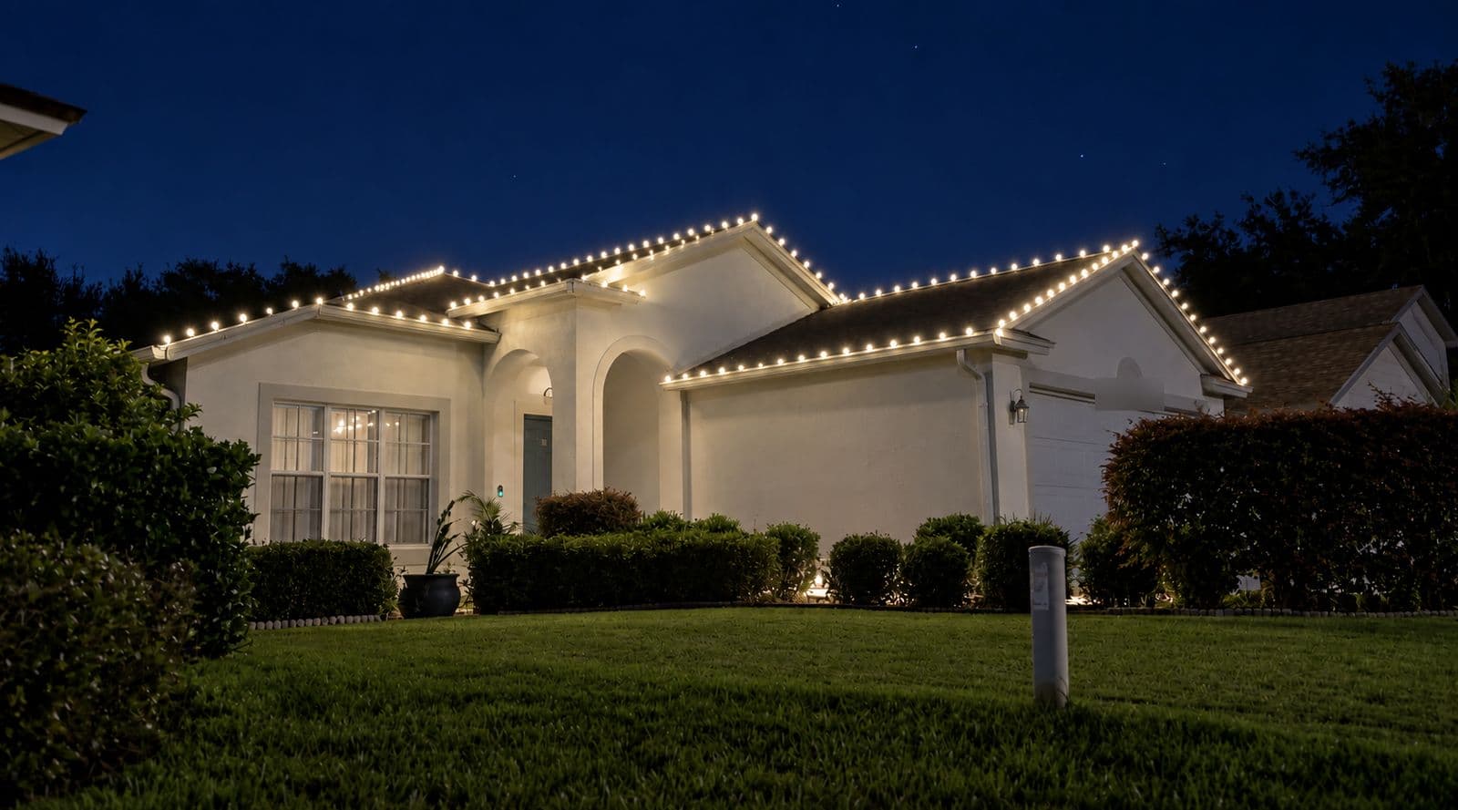 A white single-storey home at night with warm white C9 lights tracing every roofline and gable