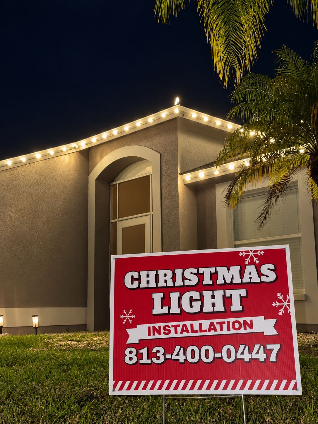 A lit roofline above an arched entry, with a red Comet Christmas Light Installation yard sign on the lawn
