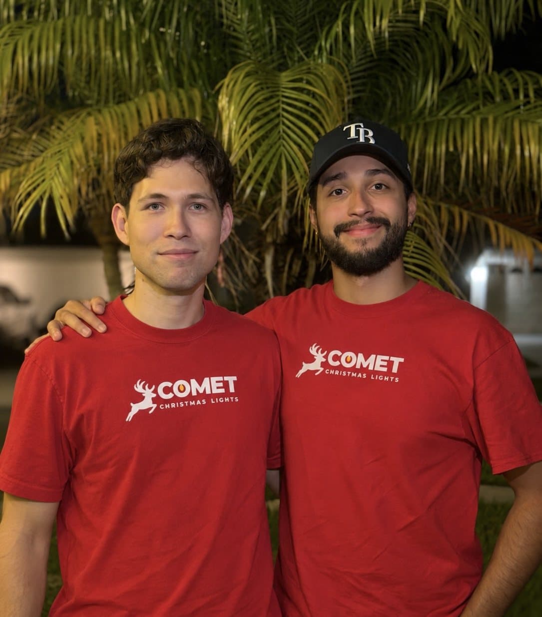 AJ and Luis of Comet Christmas Lights in red Comet T-shirts in front of a palm tree at night